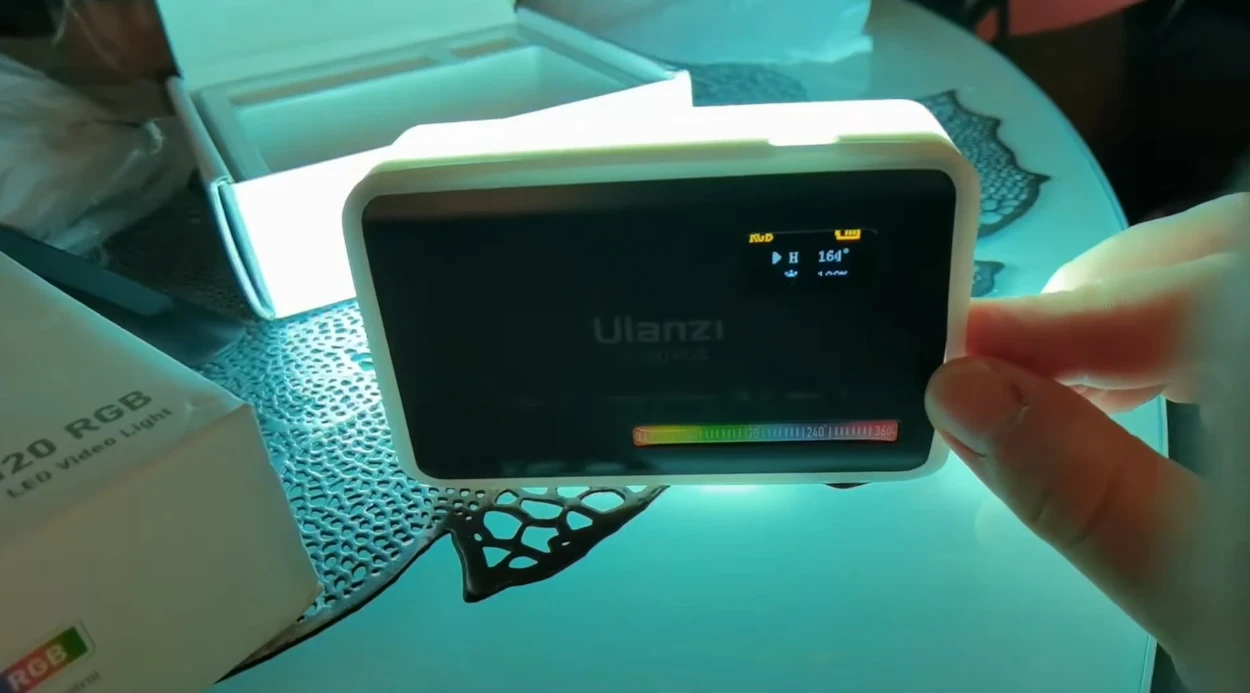 Панель Ulanzi VL120 RGB у надітому білому силіконовому розсіювачі світиться насиченим бірюзовим відтінком із відображенням параметрів H 164 градуси на екрані
